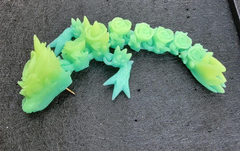 Pu&ograve; includere: Uno spillo in resina verde e blu a forma di drago con un design floreale. Il drago &egrave; arrotolato su se stesso con la testa rivolta a sinistra. Lo spillo &egrave; attaccato a un retro di spillo dorato.