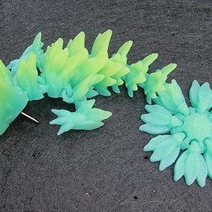 Pu&ograve; includere: Una statuetta di drago in plastica verde e blu con una schiena spinosa e una coda arrotolata in un cerchio. Il drago &egrave; fatto di molti piccoli pezzi che sono collegati tra loro.
