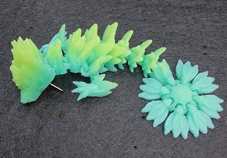 Pu&ograve; includere: Una statuetta di drago in plastica verde e blu con una schiena spinosa e una coda arrotolata in un cerchio. Il drago &egrave; fatto di molti piccoli pezzi che sono collegati tra loro.