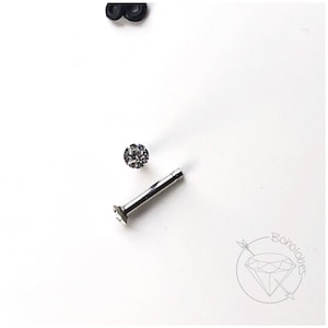 May include: A silver-colored, flat-back earring stud with a clear, round gemstone. The earring is shown with a separate gemstone and a black rubber earring back on a white background. The logo "Boholobes" is in the lower right corner.