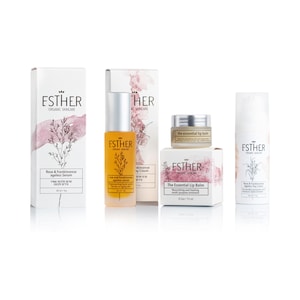 May include: A skincare set featuring Esther Organic Skincare products: a tall box and amber bottle of Rose & Frankincense Ageless Serum, a box and small jar of The Essential Lip Balm, and a white bottle of Rose & Frankincense Ageless Day Cream.