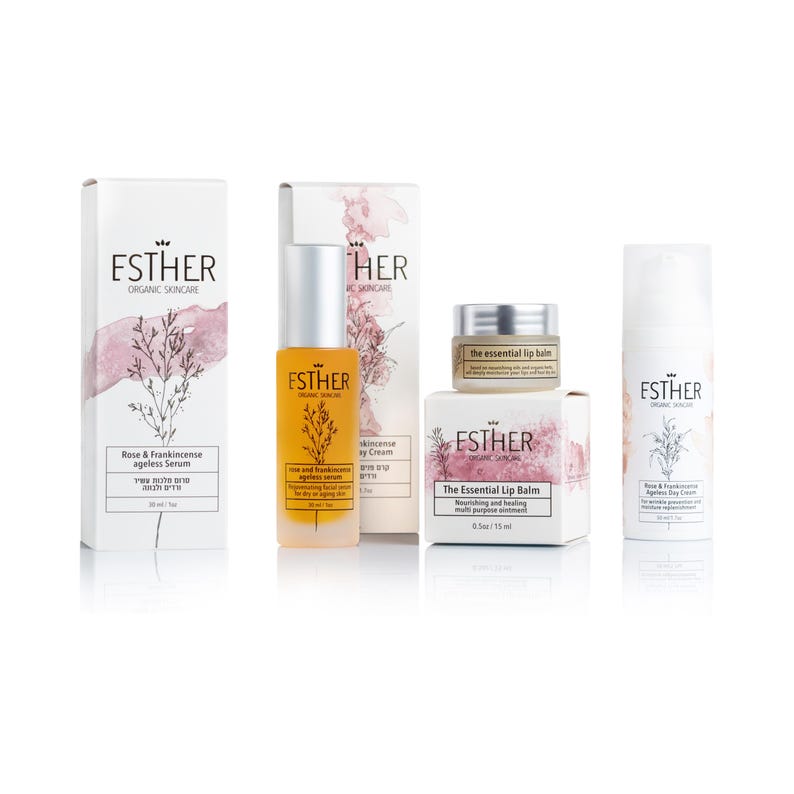 May include: A skincare set featuring Esther Organic Skincare products: a tall box and amber bottle of Rose & Frankincense Ageless Serum, a box and small jar of The Essential Lip Balm, and a white bottle of Rose & Frankincense Ageless Day Cream.