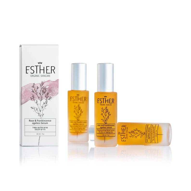 May include: Three amber glass bottles of Esther Organic Skincare Rose & Frankincense Ageless Serum, each 1 fl oz, alongside a white rectangular box featuring a botanical illustration, a pink watercolor accent, and the brand name Esther.
