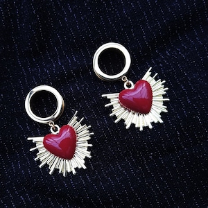 Könnte beinhalten: Ein Paar goldfarbene Ohrringe mit roten Herzanhängern. Die Herzen sind von einem goldfarbenen Dornenhalo umgeben.