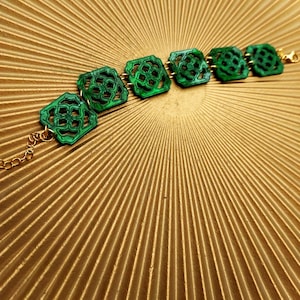 Può includere: Un braccialetto verde con intricati disegni ritagliati in ogni maglia. Il braccialetto è realizzato con una catena metallica con finitura dorata.