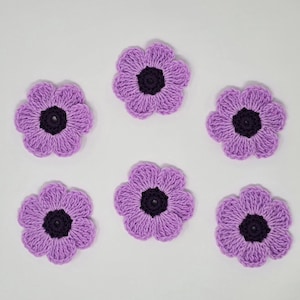 May include: Six handmade crochet flowers in a light purple shade with dark purple centres are arranged on a white background. The flowers have a textured appearance, with visible stitch details. These decorative flowers are suitable for craft projects.
