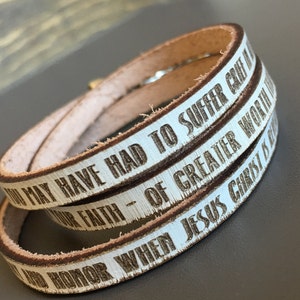 May include: A white leather wrap bracelet with the text "Your faith - of greater worth than may have had to suffer cause" and "When Jesus Christ is Lord" engraved in brown.