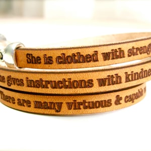 May include: A brown leather wrap bracelet with the inscription "She is clothed with strength & she gives instructions with kindness. There are many virtuous & capable"
