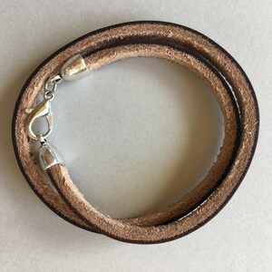 May include: A brown leather bracelet with a silver clasp. The bracelet is double-layered and has a simple design.