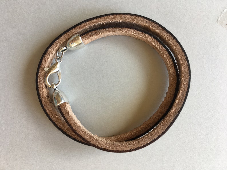 May include: A brown leather bracelet with a silver clasp. The bracelet is double-layered and has a simple design.
