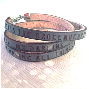 May include: A brown leather wrap bracelet with the text "Heals the broken heart. My darling. Making all things new." engraved on it.