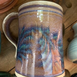 May include: A brown ceramic mug with a white rim and a blue and green glaze. The mug has a handle and is decorated with a mottled glaze.