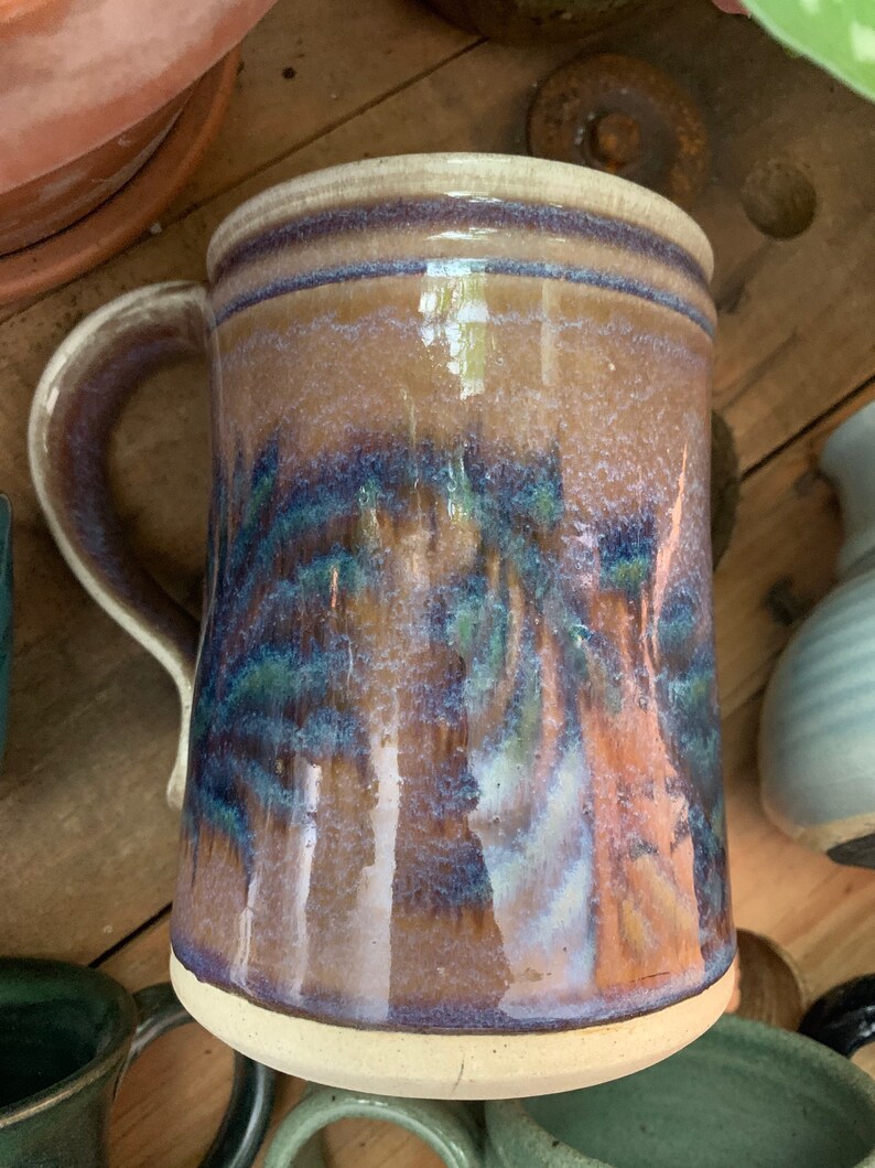 May include: A brown ceramic mug with a white rim and a blue and green glaze. The mug has a handle and is decorated with a mottled glaze.