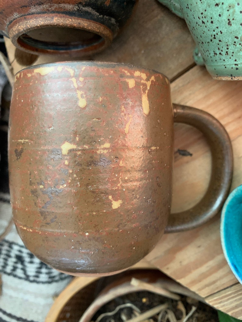 May include: A brown ceramic mug with a speckled glaze and a light brown handle. The mug has a rustic, handmade look.