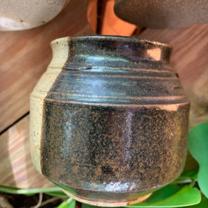 May include: A small, round ceramic pot with a black and white glaze. The pot has a speckled brown glaze on the black side.