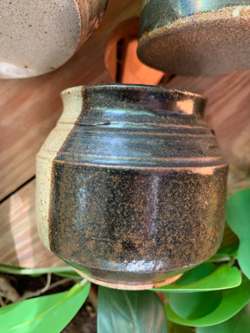 May include: A small, round ceramic pot with a black and white glaze. The pot has a speckled brown glaze on the black side.