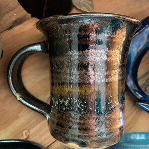 May include: A brown and black ceramic mug with a wide, rounded base and a handle. The mug has a glossy finish and a speckled glaze.