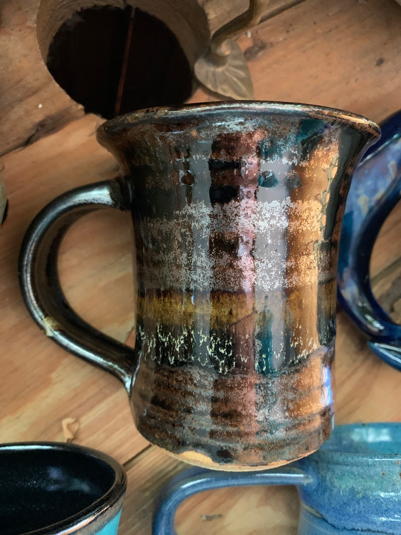 May include: A brown and black ceramic mug with a wide, rounded base and a handle. The mug has a glossy finish and a speckled glaze.