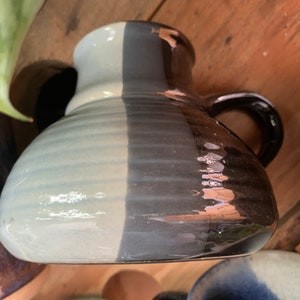 May include: A ceramic mug with a light blue and dark grey glaze. The mug has a handle and a rounded shape.