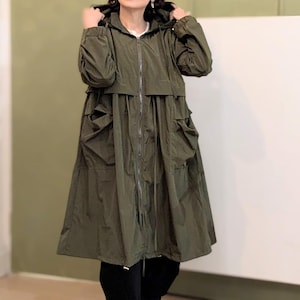Puede incluir: Una chaqueta con capucha de color verde oliva que presenta una cremallera frontal completa, mangas largas con puños elásticos, cintura con cordón ajustable y dos grandes bolsillos de parche en la parte delantera. Corte holgado y acampanado.