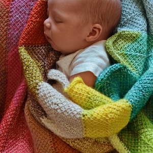 Puede incluir: Un bebé durmiendo plácidamente en una manta de crochet colorida con una variedad de colores que incluyen rosa, verde, amarillo y marrón.