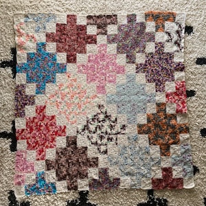 May include: A crocheted blanket with a patchwork design featuring various colors and patterns. The blanket is made up of squares with different textures and colors, including pink, blue, brown, and white.