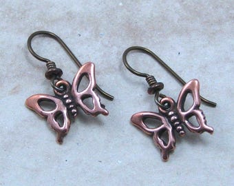 May include: A pair of copper-colored butterfly earrings. Each earring features a butterfly pendant with openwork wings and a decorative hook. The earrings are designed with a vintage aesthetic and are suitable for everyday wear.