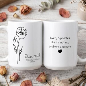May include: Two white ceramic mugs. One mug features a black poppy flower illustration and the name "Elizabeth" with "Officially Retired 2026". The other mug has the text "Every Sip tastes like it's not my problem anymore" with a black heart.