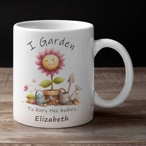 May include: White ceramic mug with a whimsical garden-themed design. The mug features a smiling flower illustration and the text "I Garden To bury the bodies Elizabeth". Includes small gardening tools and watering cans.