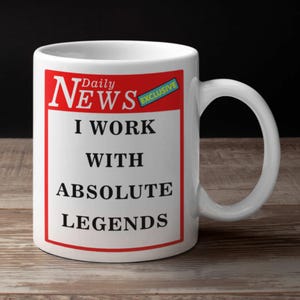 May include: White ceramic mug with a handle. The mug features a red and white design with the words "Daily News" at the top, and the text "I WORK WITH ABSOLUTE LEGENDS" in bold black letters. A small blue rectangle with the word "EXCLUSIVE" is also present.