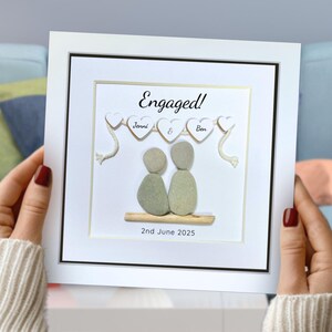 Personalised Pebble art picture in a white frame to celebrate an engagement, in a lady’s hands