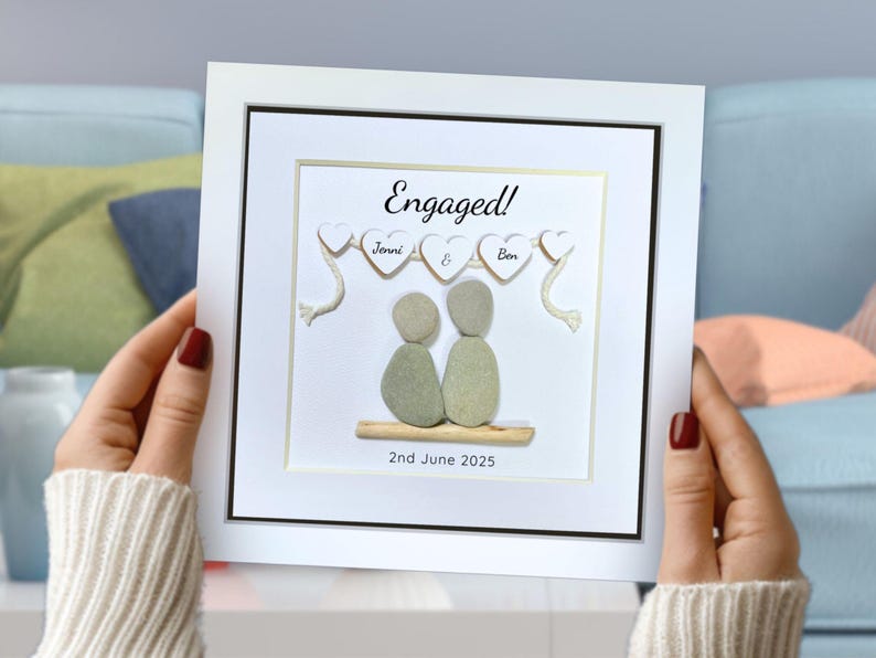 Personalised Pebble art picture in a white frame to celebrate an engagement, in a lady’s hands