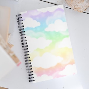 May include: A spiral bound notebook with a white cover featuring a watercolor design of pastel rainbow clouds.