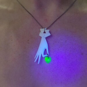 May include: A white ceramic necklace pendant shaped like a hand holding a green glass apple. The pendant is on a silver chain.