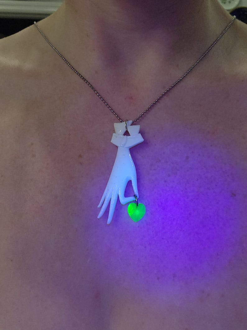 May include: A white ceramic necklace pendant shaped like a hand holding a green glass apple. The pendant is on a silver chain.