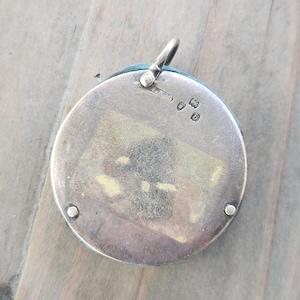 Pu&ograve; includere: Un ciondolo rotondo in argento con un bordo in tessuto turchese. Presenta un piccolo anello nella parte superiore per una catena. Il retro del ciondolo presenta marchi e una piccola finestra rettangolare.