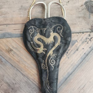 Peut inclure: Un étui à ciseaux en tissu noir avec une chaîne dorée et un motif de dragon brodé en or.
