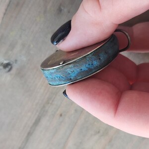 Pu&ograve; includere: Un piccolo cuscino per spilli rotondo antico con una cornice in metallo color argento e un cuscino in tessuto blu. Il cuscino ha un motivo cucito decorativo. Un piccolo anello di metallo &egrave; attaccato in alto.