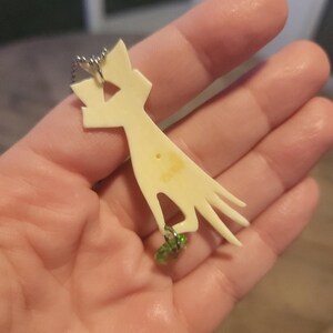 May include: A white bone pendant shaped like a hand with a green glass bead charm attached to the chain.