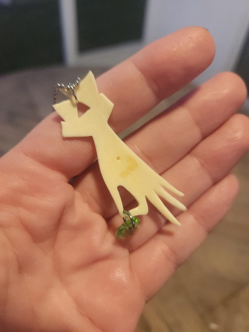 May include: A white bone pendant shaped like a hand with a green glass bead charm attached to the chain.