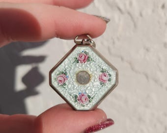 May include: A silver pendant with a white enamel background and pink and green floral details. The pendant is in the shape of an octagon.
