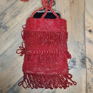 May include: A red beaded bag with a long fringe. The bag has a small pocket on the front that can hold a phone.