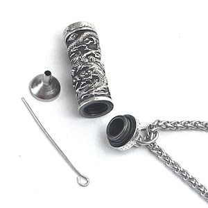 May include: Silver dragon pendant necklace with a small funnel and a thin metal rod. The pendant is a cylinder with a screw-on top and a dragon design.