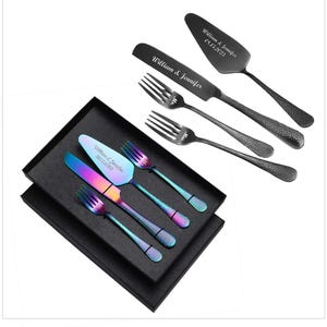 May include: A set of four black and iridescent cake cutting utensils in a black box. The utensils include two cake servers and two forks. The cake servers are engraved with the text "William & Jennifer" and the date "05.21.2023".