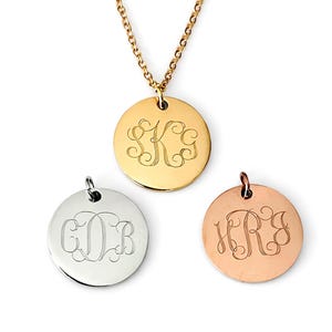 May include: Gold, silver, and rose gold monogrammed pendant necklaces. Each round pendant features a unique, engraved monogram in an elegant script. The gold necklace is on a chain. The pendants are displayed on a white background.