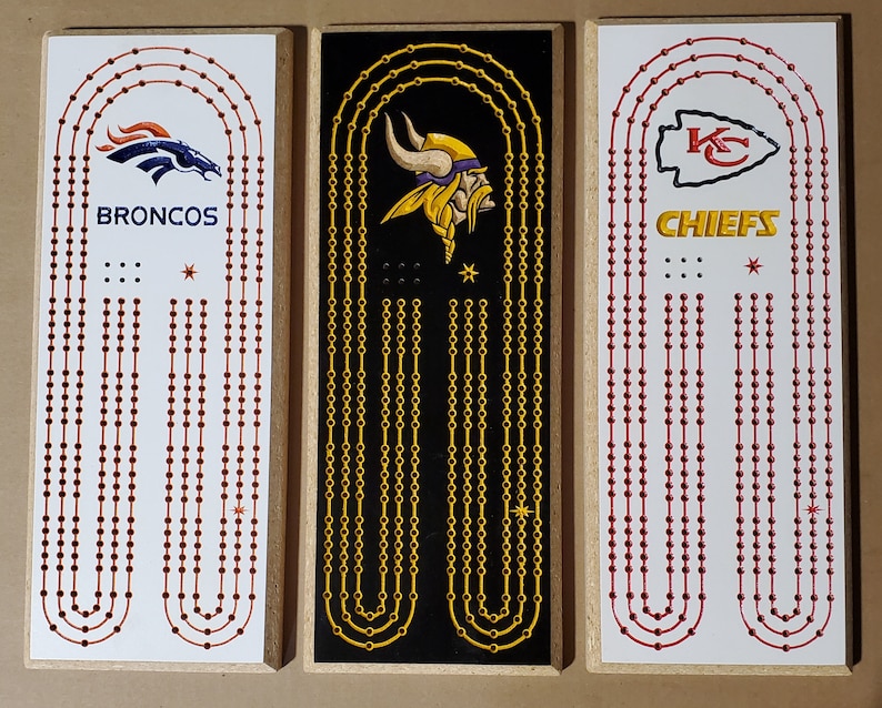 May include: Three wooden game boards with different NFL team logos. The boards are white with red, orange, and gold dots. The logos are the Denver Broncos, Minnesota Vikings, and Kansas City Chiefs.