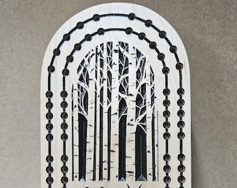 Peut inclure: Jeu de cribbage en bois avec un motif de bouleau. La planche de couleur claire présente une silhouette d'arbre noire au centre. Des rangées arquées de trous pour les chevilles entourent le motif de l'arbre. Une étoile et des points sont en bas.