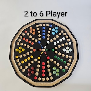 May include: An octagonal board game with the text 2 to 6 Player, featuring a black surface with circular indentations arranged in a star pattern. The board includes sets of colored marbles in orange, blue, white, green, red, and yellow.