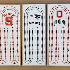 May include: Three wooden game boards with red, white, and blue team logos. The boards feature the logos for Syracuse, the New England Patriots, and Ohio State. Each board has a white background with red and blue dots.