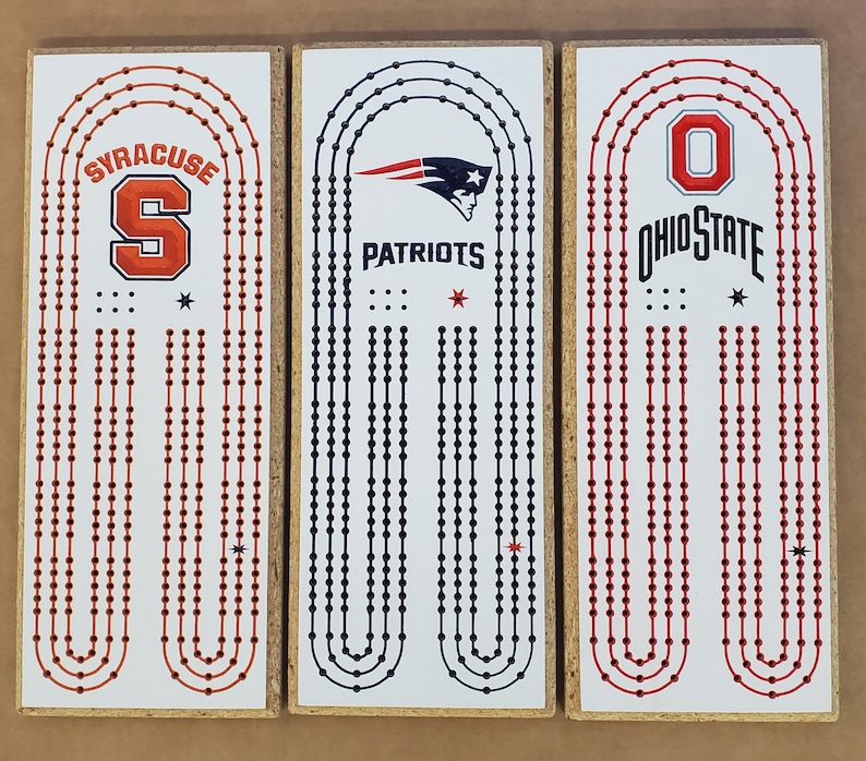 May include: Three wooden game boards with red, white, and blue team logos. The boards feature the logos for Syracuse, the New England Patriots, and Ohio State. Each board has a white background with red and blue dots.